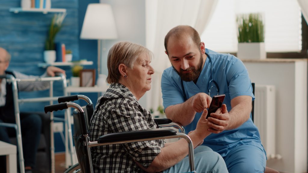 Man nurse teaching retired woman with disability to use smartphone